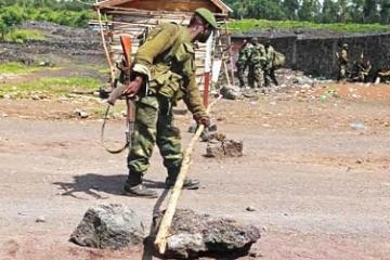 Une vue d'un soldat FARDC qui utilise un bâton en bois pour barrer la route, dans une zone ouverte de la RDC. 